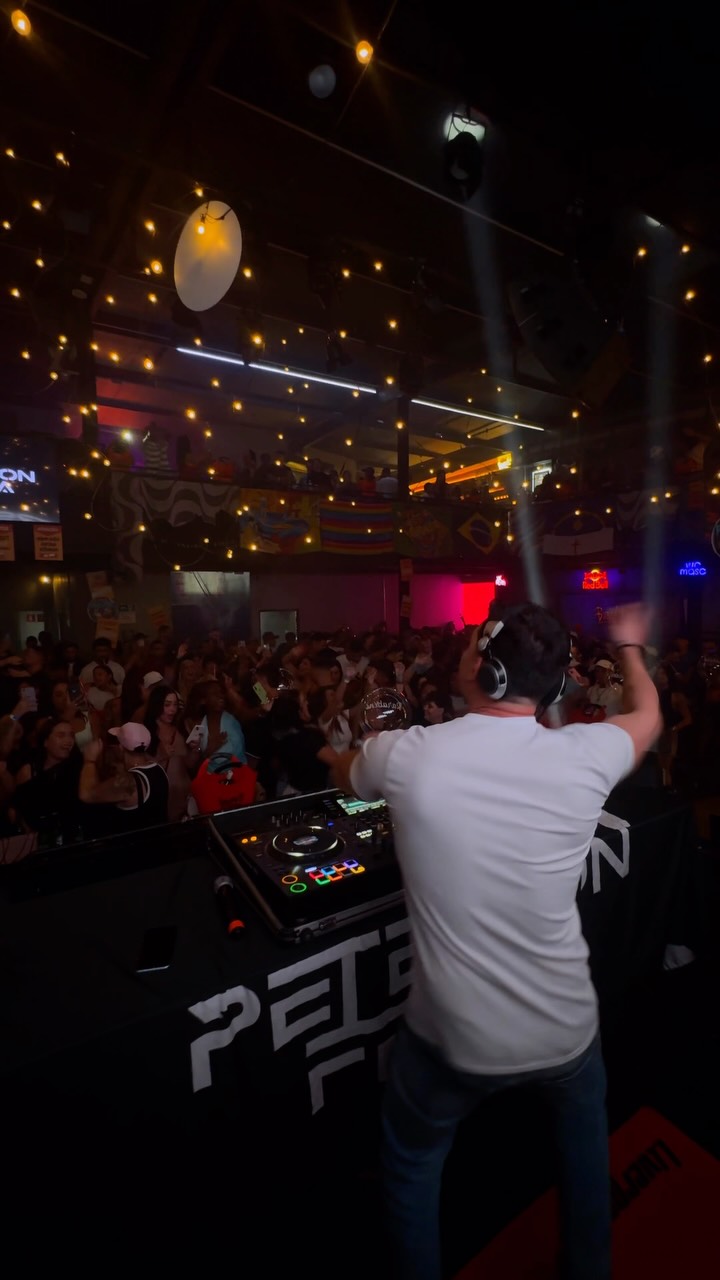 DJ no palco e público reunido na Bronks, sob as luzes da casa